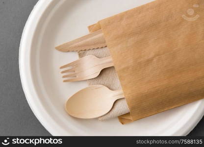 cutlery, recycling and eco friendly concept - set of wooden spoon, fork and knife on paper plate on grey background. wooden spoon, fork and knife on paper plate