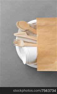 cutlery, recycling and eco friendly concept - set of wooden spoons, forks and knives with paper cups on plate on grey background. wooden spoons, forks and knives on paper plate