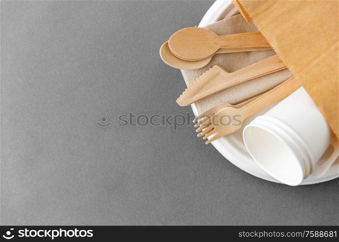 cutlery, recycling and eco friendly concept - set of wooden spoons, forks and knives with paper cups on plate on grey background. wooden spoons, forks and knives on paper plate
