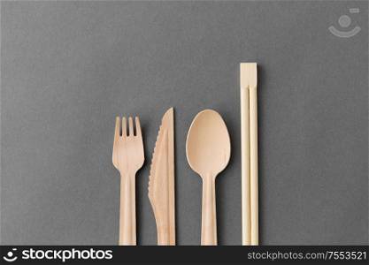 cutlery, recycling and eco friendly concept - wooden disposable spoon, fork, knife and chopsticks on grey background. wooden spoon, fork, knife and chopsticks