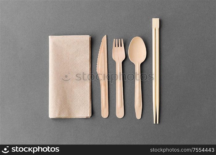 cutlery, recycling and eco friendly concept - wooden disposable spoon, fork, knife with chopsticks and paper napkin on grey background. wooden spoon, fork, knife and chopsticks