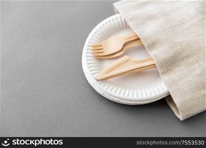 cutlery, recycling and eco friendly concept - wooden forks and knives on paper plates and canvas napkin on grey background. wooden forks and knives on paper plates and napkin