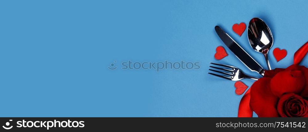 Cutlery set tied with silk ribbon and hearts on blue background Valentine day dinner concept. Cutlery set and hearts