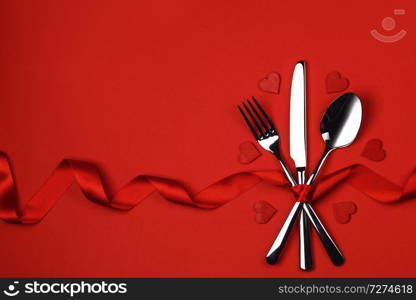 Cutlery set tied with silk ribbon and hearts on red background Valentine day dinner concept. Cutlery set and hearts