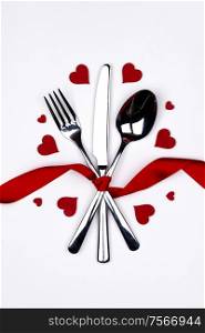 Cutlery set tied with silk ribbon and hearts on white background Valentine day dinner concept. Cutlery set and hearts
