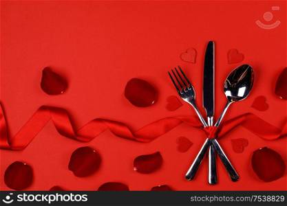 Cutlery set tied with silk ribbon rose flower petals and hearts on red background Valentine day dinner concept. Cutlery set rose petals and hearts