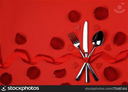 Cutlery set tied with silk ribbon rose flower petals and hearts on red background Valentine day dinner concept. Cutlery set rose petals and hearts