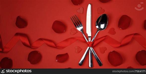 Cutlery set tied with silk ribbon rose petals and hearts on red background Valentine day romantic dinner concept. Romantic dinner concept