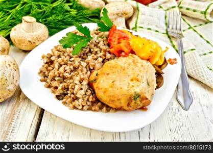 Cutlet of turkey meat with buckwheat, mushrooms, tomato and yellow pepper in a dish, parsley, a towel and a fork on the background of wooden boards