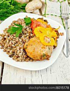 Cutlet of turkey meat with buckwheat, mushrooms, tomatoes and peppers in the dish, parsley, a towel and a fork on the background of wooden boards