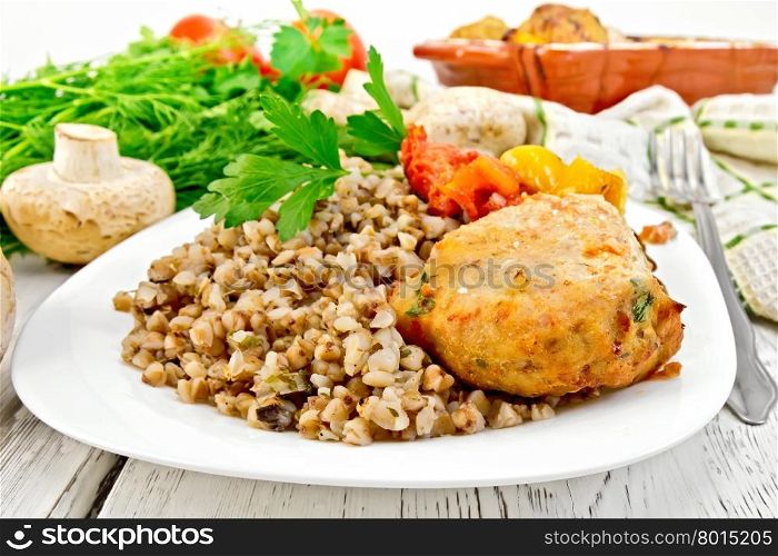 Cutlet of turkey meat with buckwheat, mushrooms, tomatoes and peppers in the dish, parsley, a towel and a fork on the background light wooden boards