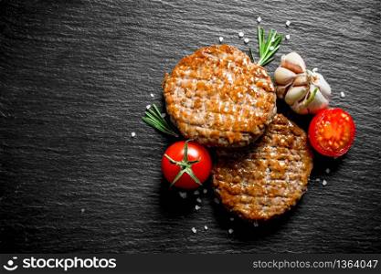 Cutlets with tomatoes,garlic and rosemary. On black rustic background. Cutlets with tomatoes,garlic and rosemary.