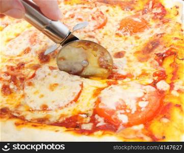 Cutting a cheese and tomato pizza with a pizza-wheel