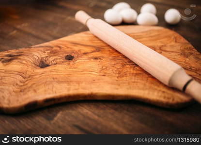 Cutting board, rolling pin and eggs on wooden background closeup view. Homemade food cooking concept. Dough baking