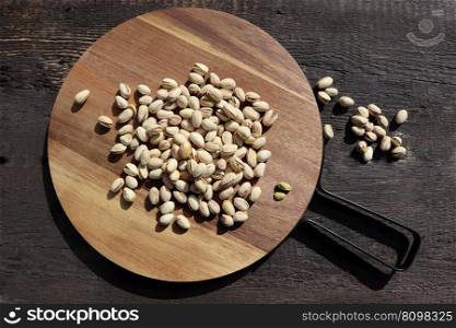 Cutting board with tasty pistachio nuts on dark rustic brown wooden background .. Cutting board with tasty pistachio nuts on dark rustic brown wooden background