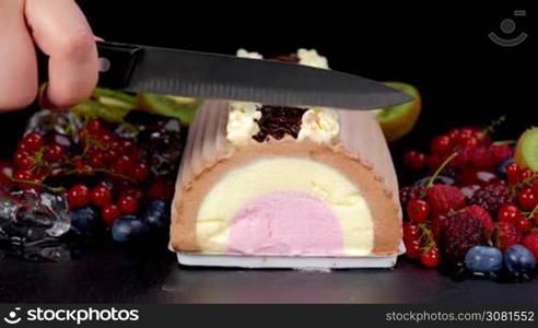 Cutting chocolate vanilla strawberry ice cream roll with berries fruits. Closeup