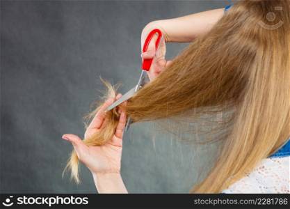 Cutting coiffure and new look. Part body blonde woman cut her long straight hair. Female hands with red scissors making modern hairstyle.. Blonde woman cutting her hair.
