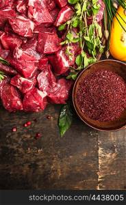 cutting raw meat with spices and fresh herbs , ingredients for goulash cooking on rustic wooden background, top view, place for text
