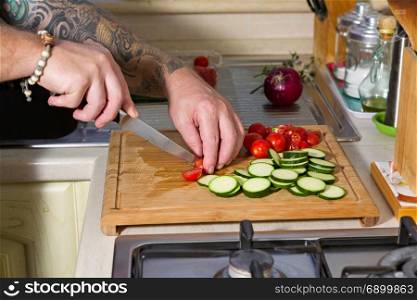 Cutting the zucchini, cherry tomatoes and red onion over a chopping board. Whole farfalle pasta with zucchini, cherry tomatoes and red onion