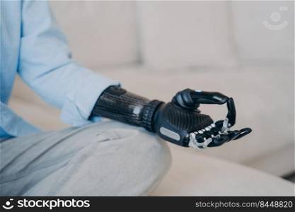 Cyber hand of disabled person which is sitting in lotus pose on couch. Myoelectric bionic prosthesis. Artificial limb with nervous sensor control. Robotic arm and hand in meditation.. Cyber hand of disabled person which is sitting in lotus pose on couch. Robotic arm in meditation.