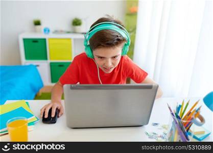 cyberbullying, gaming and people concept - boy in headphones playing video game on laptop computer at home. boy in headphones playing video game on laptop
