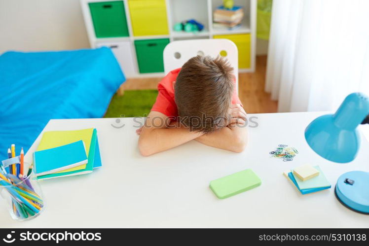 cyberbullying, technology and people concept - tired or sad student boy with smartphone lying on desk at home suffering from bullying. tired or sad student boy with smartphone at home