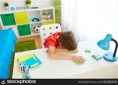cyberbullying, technology and people concept - tired or sad student boy with smartphone lying on desk at home suffering from bullying. tired or sad student boy with smartphone at home