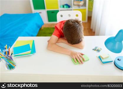 cyberbullying, technology and people concept - tired or sad student boy with smartphone lying on desk at home suffering from bullying. tired or sad student boy with smartphone at home