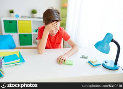 cyberbullying, technology and people concept - tired or suffering from headache or bullying student boy with smartphone sitting at desk at home. tired student boy with smartphone at home