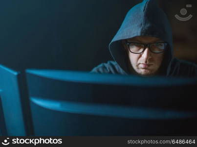 cybercrime, hacking and technology concept - close up of hooded hacker in glasses at computer monitor. close up of hacker in hood at computer monitor. close up of hacker in hood at computer monitor