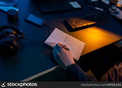 cybercrime, hacking and technology concept - close up of male hacker in dark room writing to notebook and using computer virus program for cyber attack. hacker using computer virus for cyber attack