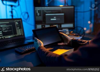 cybercrime, hacking and technology concept - close up of male hacker in dark room with tablet pc using computer virus program for cyber attack. hacker using tablet pc computer for cyber attack