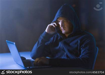 cybercrime, hacking and technology concept - male hacker in dark room networking or using laptop computer for cyber attack and calling on cellphone. hacker with laptop calling on cellphone. hacker with laptop calling on cellphone