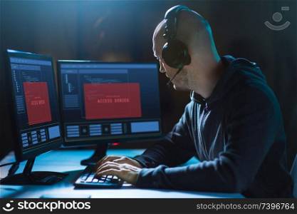 cybercrime, hacking and technology concept - male hacker in headset with access denied messages on computer&rsquo;s screens wiretapping or using computer virus program for cyber attack in dark room. hacker with access denied messages on computers