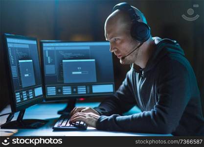 cybercrime, hacking and technology concept - male hacker in headset with progress loading bar on computer screen wiretapping or using virus program for cyber attack in dark room. hacker with computer and headset in dark room