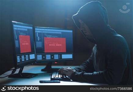 cybercrime, hacking and technology concept - male hacker with access denied message on computer screen using virus program for cyber attack in dark room. hacker with access denied messages on computer