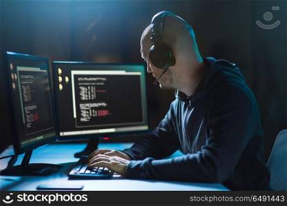 cybercrime, hacking and technology concept - male hacker with headphones and coding on laptop computer screen wiretapping or using computer virus program for cyber attack in dark room. hacker with coding on laptop computer in dark room. hacker with coding on laptop computer in dark room