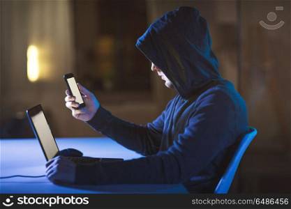 cybercrime, hacking and technology concept - male hacker with laptop computer and smartphone in dark room. hacker with laptop and smartphone in dark room. hacker with laptop and smartphone in dark room