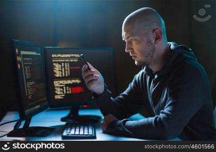 cybercrime, hacking and technology concept - male hacker with smartphone and coding on computers screen in dark room. hacker with smartphone and computers in dark room. hacker with smartphone and computers in dark room