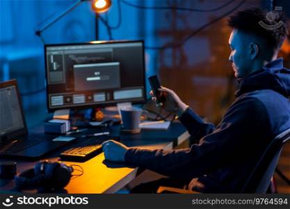 cybercrime, hacking and technology concept - male hacker with smartphone using computer virus program for cyber attack in dark room. hacker with smartphone and computers in dark room