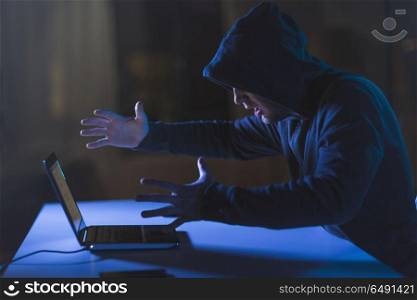 cybercrime, hacking and technology crime - angry male hacker with laptop computer in dark room. angry hacker with laptop computer in dark room. angry hacker with laptop computer in dark room