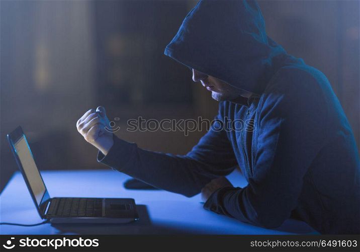 cybercrime, hacking and technology crime - male hacker showing fist to laptop computer in dark room. hacker showing fist to laptop in dark room. hacker showing fist to laptop in dark room