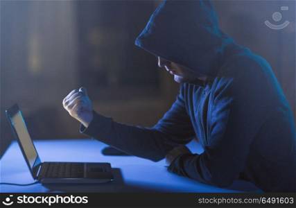 cybercrime, hacking and technology crime - male hacker showing fist to laptop computer in dark room. hacker showing fist to laptop in dark room. hacker showing fist to laptop in dark room