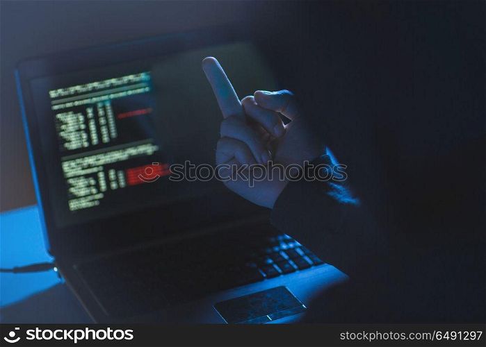 cybercrime, hacking and technology crime - male hacker showing middle finger to laptop computer in dark room. hacker showing middle finger to laptop. hacker showing middle finger to laptop