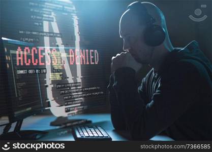 cybercrime, hacking, wiretapping and technology concept - male hacker in headphones with access denied message on computer screen using virus program for cyber attack in dark room. hacker with access denied messages on computer