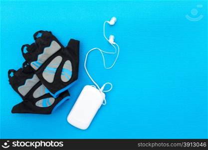 Cycling concept. Bicycle gloves and mp player on blue background.