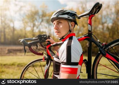 Cyclist in helmet and sportswear keeps the bike on shoulder, cycling on asphalt road. Male sportsman rides on bicycle. Workout on bike path
