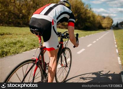 Cyclist in helmet and sportswear rides on bicycle, back view. Workout on bike path, cycling
