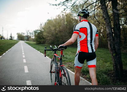 Cyclist in helmet and sportswear rides on bicycle, back view. Workout on bike path, cycling. Cyclist in helmet and sportswear rides on bicycle