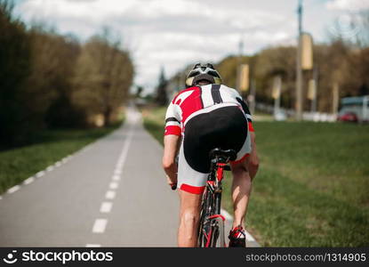 Cyclist in helmet and sportswear rides on bicycle, side view. Workout on bike path, cycling. Cyclist rides on bicycle, side view